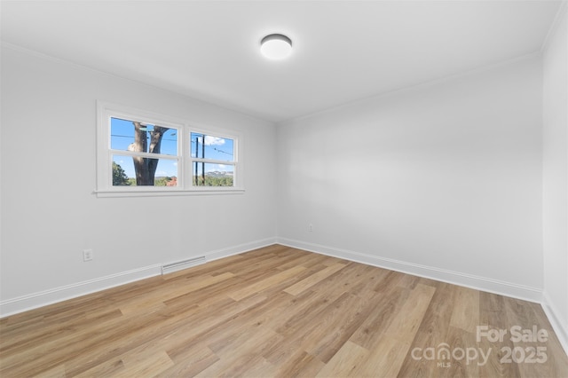 empty room featuring crown molding, light wood-style floors, visible vents, and baseboards