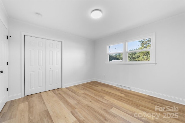 unfurnished bedroom featuring light wood-style flooring, baseboards, visible vents, and a closet