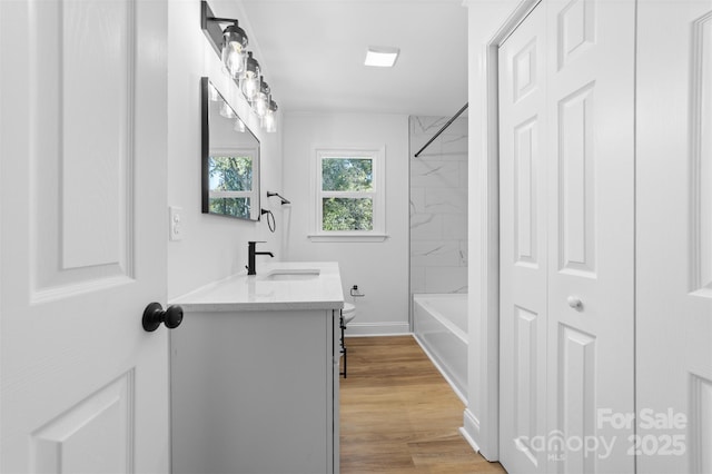 bathroom with vanity, washtub / shower combination, wood finished floors, baseboards, and toilet