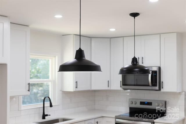 kitchen featuring a sink, backsplash, white cabinetry, appliances with stainless steel finishes, and hanging light fixtures