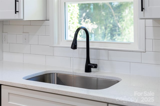 interior details featuring light stone counters, decorative backsplash, white cabinets, and a sink