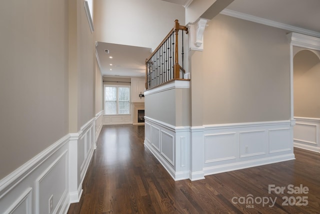 hall with decorative columns, crown molding, and dark wood-type flooring