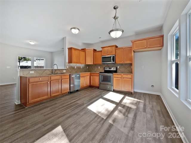 kitchen featuring kitchen peninsula, hardwood / wood-style floors, sink, appliances with stainless steel finishes, and tasteful backsplash