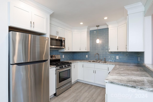 kitchen featuring appliances with stainless steel finishes, white cabinetry, ornamental molding, decorative light fixtures, and sink