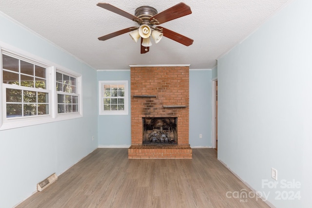 unfurnished living room featuring a fireplace, light hardwood / wood-style flooring, crown molding, a textured ceiling, and ceiling fan