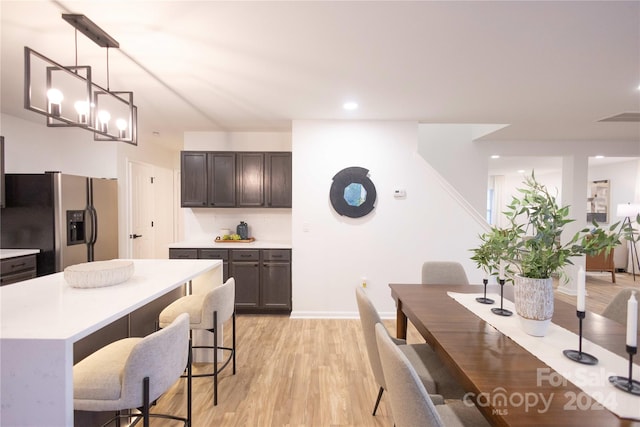 kitchen featuring light wood-type flooring, a breakfast bar area, stainless steel fridge, pendant lighting, and an inviting chandelier