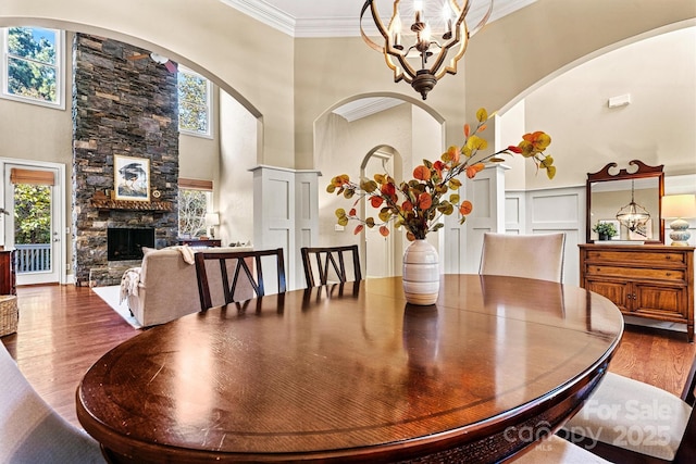 dining space with ornamental molding, a high ceiling, an inviting chandelier, a fireplace, and hardwood / wood-style floors