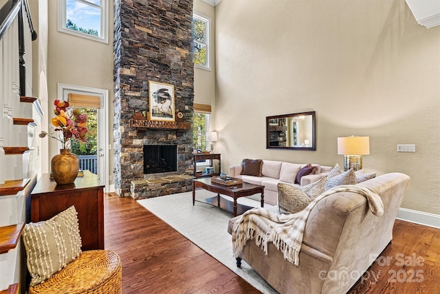 living room with a stone fireplace, ornamental molding, dark wood-type flooring, and a towering ceiling