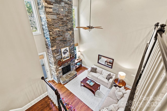 living room with a fireplace, wood-type flooring, a towering ceiling, and ceiling fan