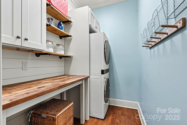 clothes washing area featuring dark hardwood / wood-style floors, cabinets, ornamental molding, and stacked washer and dryer