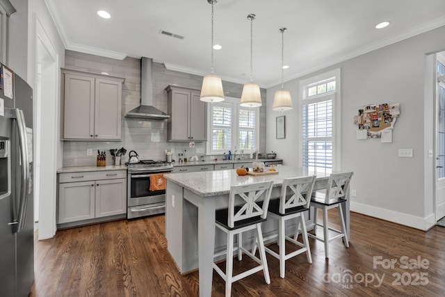 kitchen featuring hanging light fixtures, gray cabinets, a kitchen island, stainless steel appliances, and wall chimney range hood