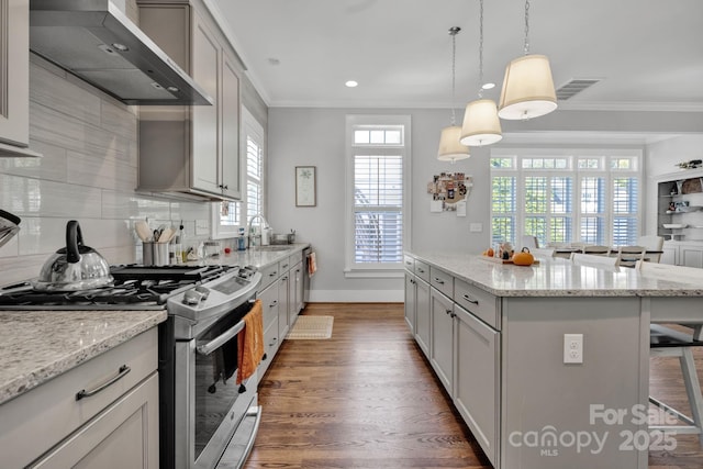 kitchen featuring wall chimney exhaust hood, a breakfast bar, crown molding, stainless steel range with gas stovetop, and a kitchen island