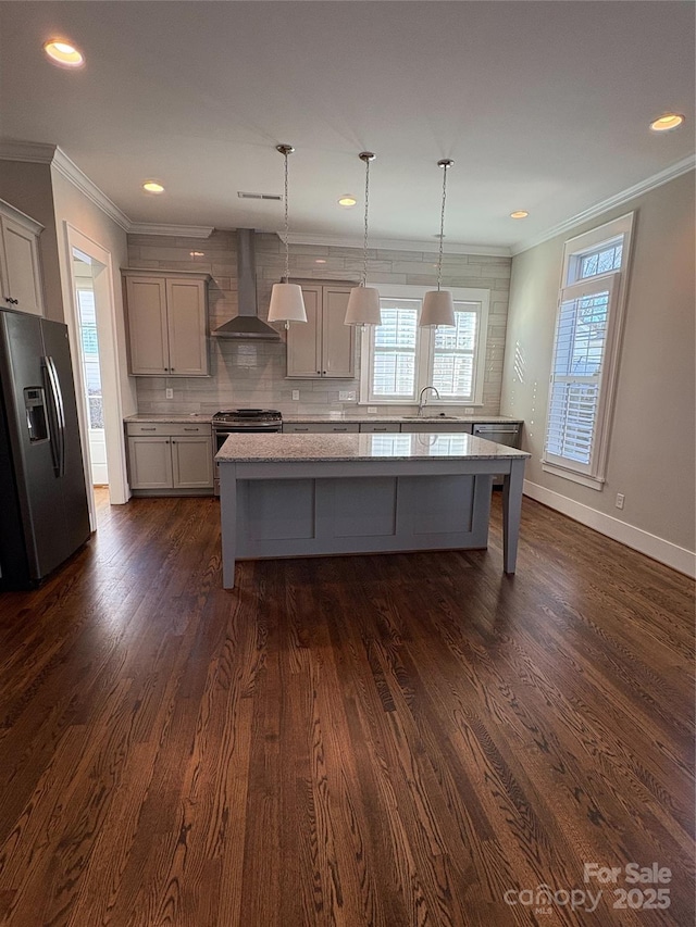 kitchen with pendant lighting, stainless steel appliances, sink, and wall chimney range hood