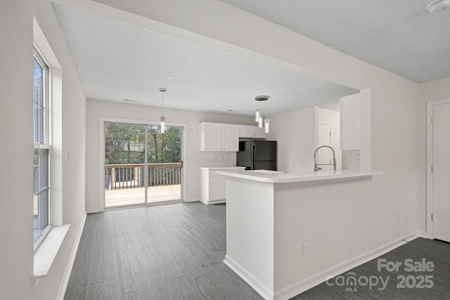 kitchen featuring black fridge, white cabinetry, kitchen peninsula, and hanging light fixtures