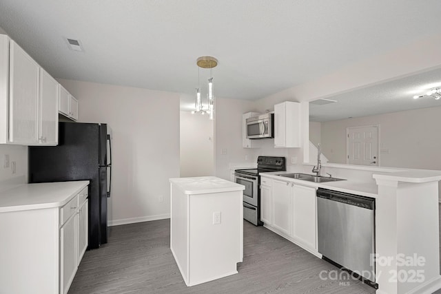 kitchen featuring kitchen peninsula, stainless steel appliances, a center island, decorative light fixtures, and sink