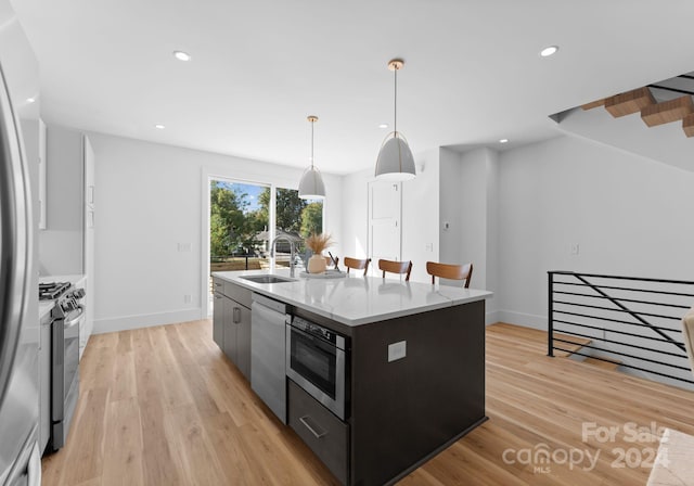 kitchen with a center island with sink, sink, hanging light fixtures, and stainless steel appliances