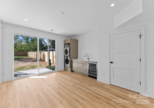 bar featuring wine cooler, sink, light hardwood / wood-style flooring, and stacked washer / dryer