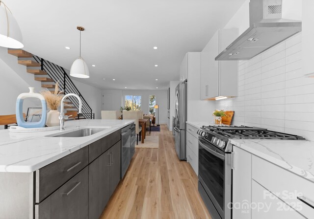 kitchen with appliances with stainless steel finishes, pendant lighting, sink, white cabinets, and wall chimney range hood