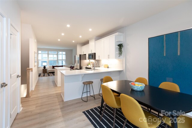 kitchen with sink, light hardwood / wood-style flooring, appliances with stainless steel finishes, kitchen peninsula, and white cabinets