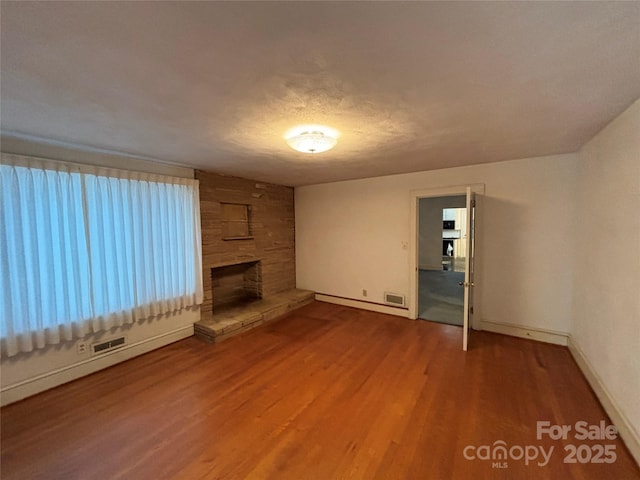 unfurnished living room featuring a stone fireplace, wood-type flooring, a textured ceiling, and baseboard heating