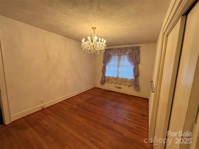 spare room with a textured ceiling, dark hardwood / wood-style flooring, and a notable chandelier