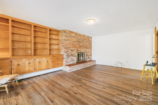 unfurnished living room with baseboard heating, a fireplace, built in features, and hardwood / wood-style flooring