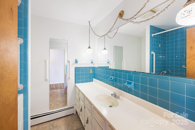 bathroom featuring baseboard heating, vanity, decorative backsplash, and a tile shower