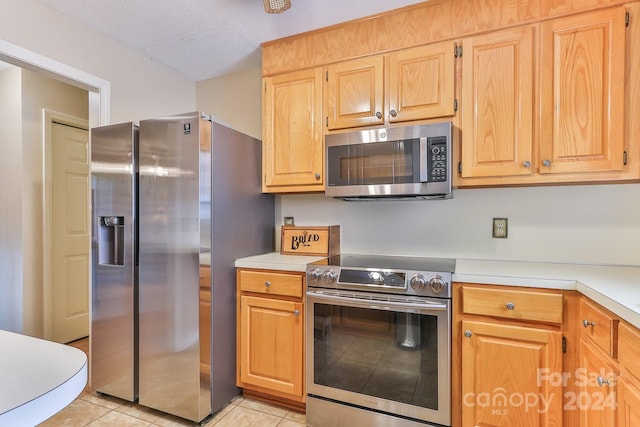 kitchen with a textured ceiling, light tile patterned flooring, and stainless steel appliances