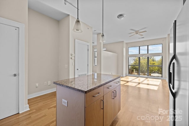 kitchen featuring light hardwood / wood-style flooring, hanging light fixtures, stainless steel refrigerator with ice dispenser, a kitchen island, and dark stone counters