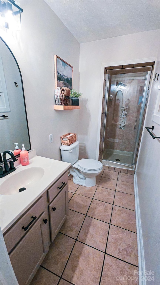 bathroom featuring a textured ceiling, toilet, a shower with shower door, vanity, and tile patterned flooring