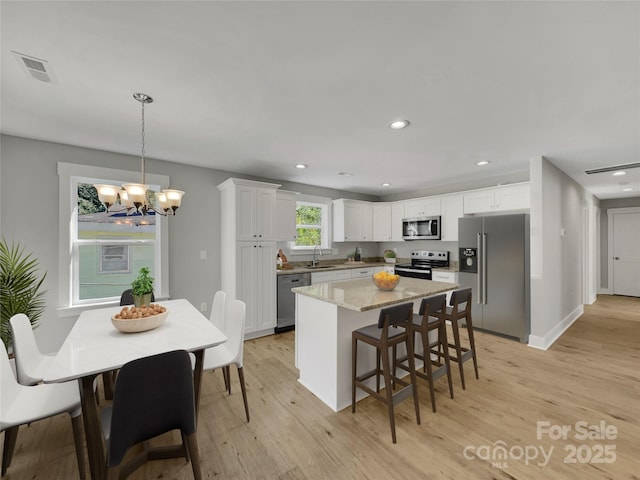 kitchen featuring an inviting chandelier, white cabinets, light stone countertops, decorative light fixtures, and stainless steel appliances