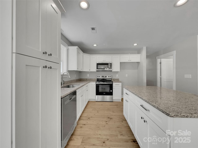 kitchen featuring light stone countertops, white cabinetry, sink, stainless steel appliances, and light wood-type flooring