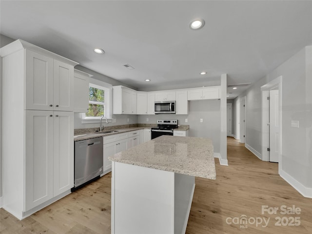 kitchen with a center island, white cabinets, sink, appliances with stainless steel finishes, and light stone counters