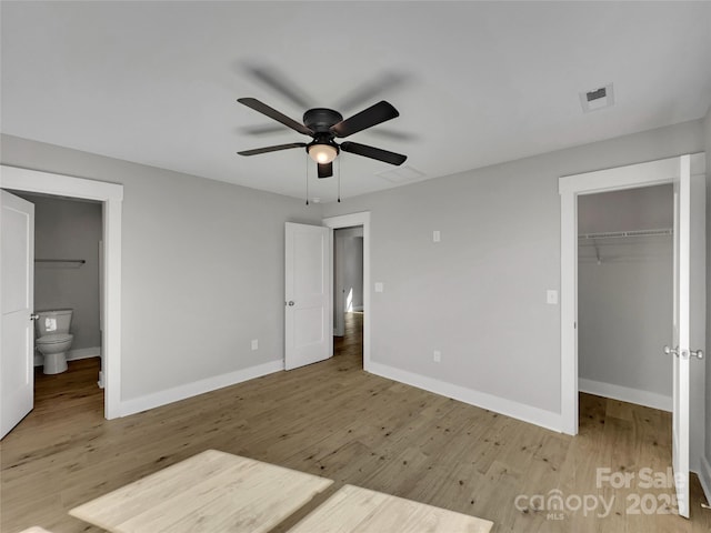 unfurnished bedroom featuring ensuite bathroom, a walk in closet, ceiling fan, light wood-type flooring, and a closet