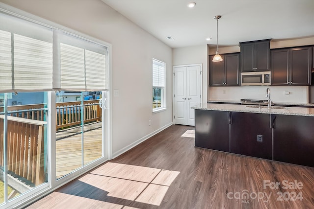 kitchen with light stone countertops, sink, hanging light fixtures, dark brown cabinetry, and dark hardwood / wood-style floors