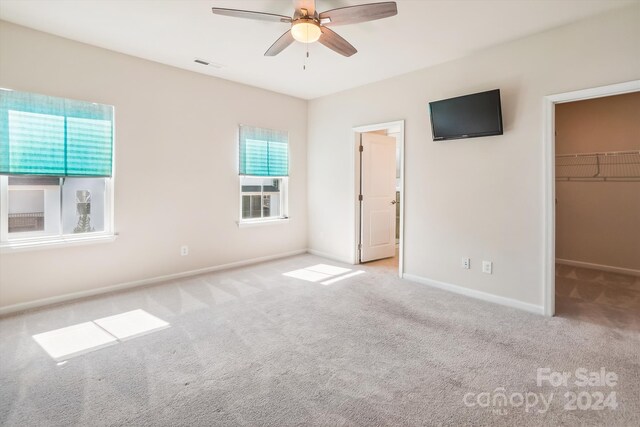 unfurnished bedroom with a spacious closet, ceiling fan, a closet, and light carpet