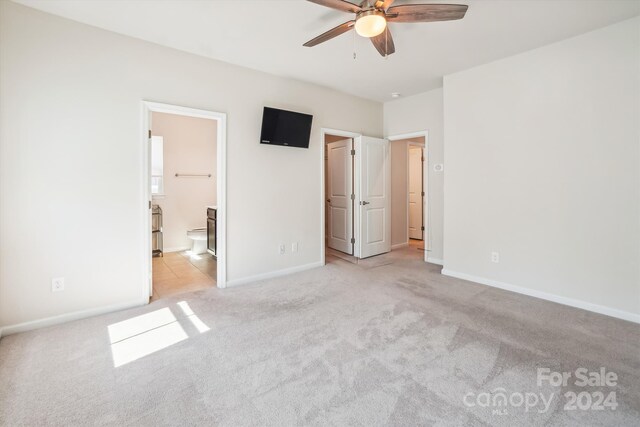 unfurnished bedroom featuring ensuite bathroom, light colored carpet, and ceiling fan