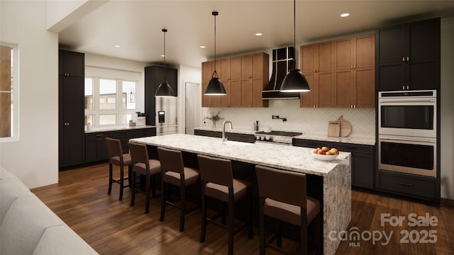 kitchen with decorative backsplash, a center island with sink, hanging light fixtures, and light stone counters