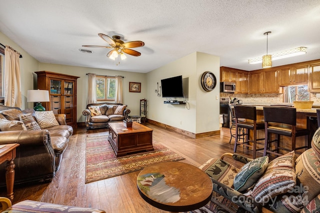 living room with a textured ceiling, light wood-type flooring, and ceiling fan