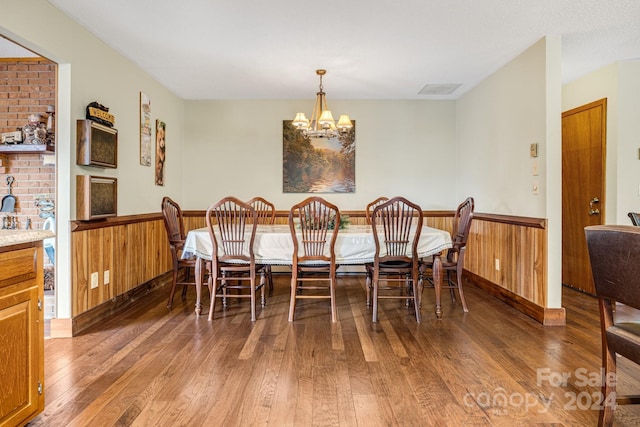 dining area with wood walls, an inviting chandelier, and dark hardwood / wood-style floors