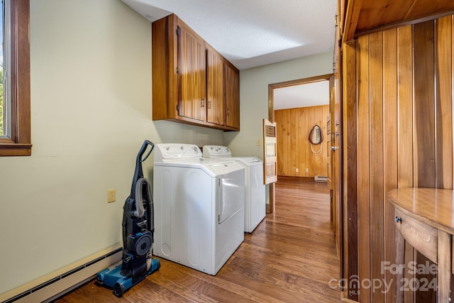 laundry room with dark hardwood / wood-style floors, wooden walls, a baseboard heating unit, cabinets, and washing machine and clothes dryer