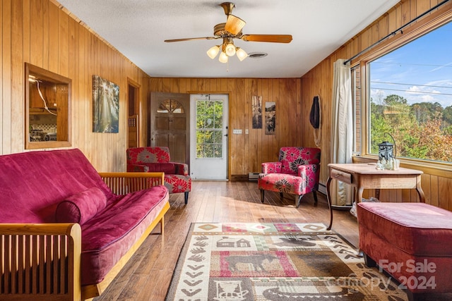 living area with a baseboard radiator, hardwood / wood-style floors, ceiling fan, and wooden walls