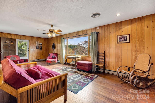 living room with a textured ceiling, wooden walls, wood-type flooring, and ceiling fan