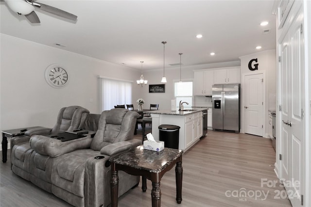 living room with light hardwood / wood-style flooring, ornamental molding, sink, and ceiling fan with notable chandelier