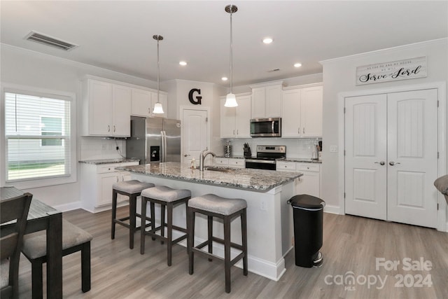 kitchen featuring white cabinets, a kitchen island with sink, stainless steel appliances, and hanging light fixtures