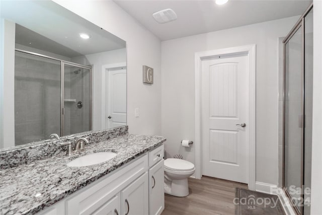 bathroom featuring vanity, hardwood / wood-style flooring, toilet, and a shower with door