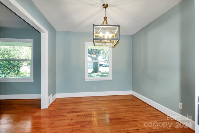 unfurnished room featuring hardwood / wood-style floors, a chandelier, and plenty of natural light