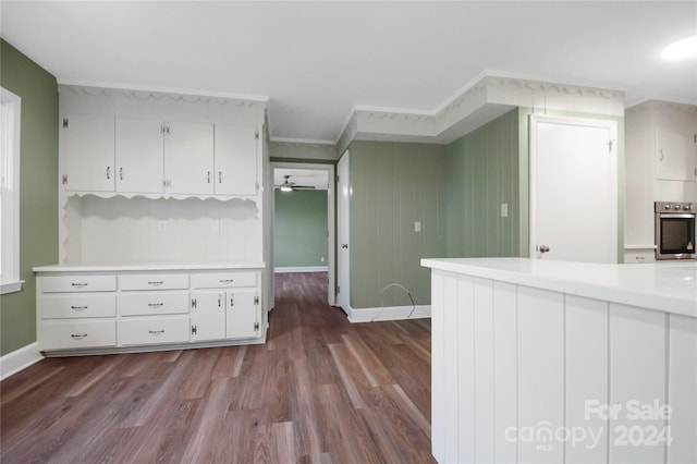 kitchen with wood-type flooring, stainless steel oven, white cabinetry, ceiling fan, and ornamental molding