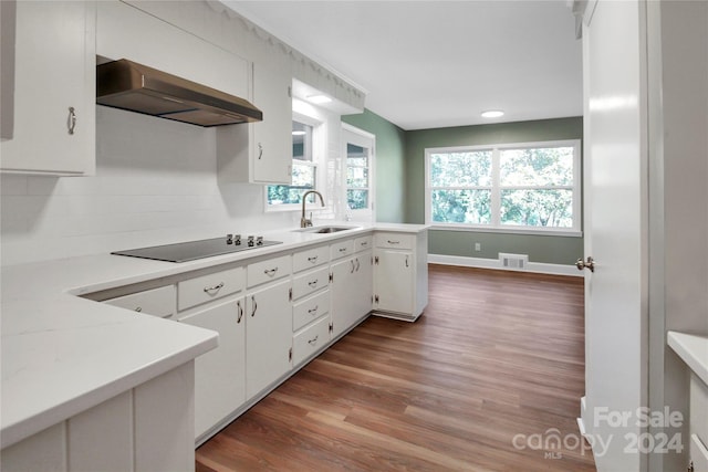 kitchen featuring white cabinetry, wood-type flooring, black electric cooktop, wall chimney exhaust hood, and sink