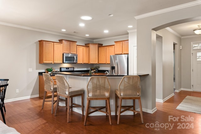 kitchen featuring dark wood-type flooring, kitchen peninsula, crown molding, a breakfast bar, and appliances with stainless steel finishes